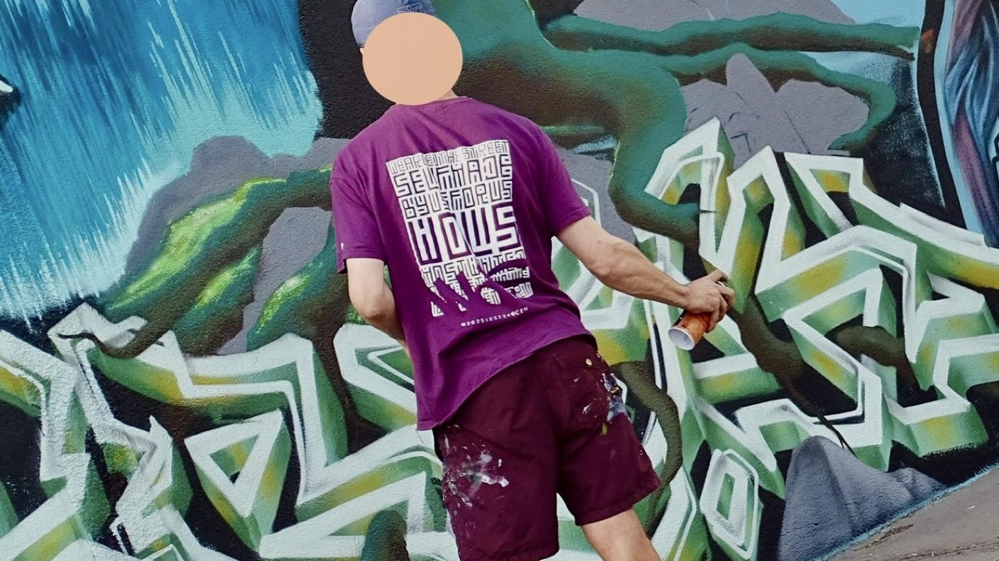Artiste peignant un décor de paysage stylisé avec graffiti sur un mur extérieur