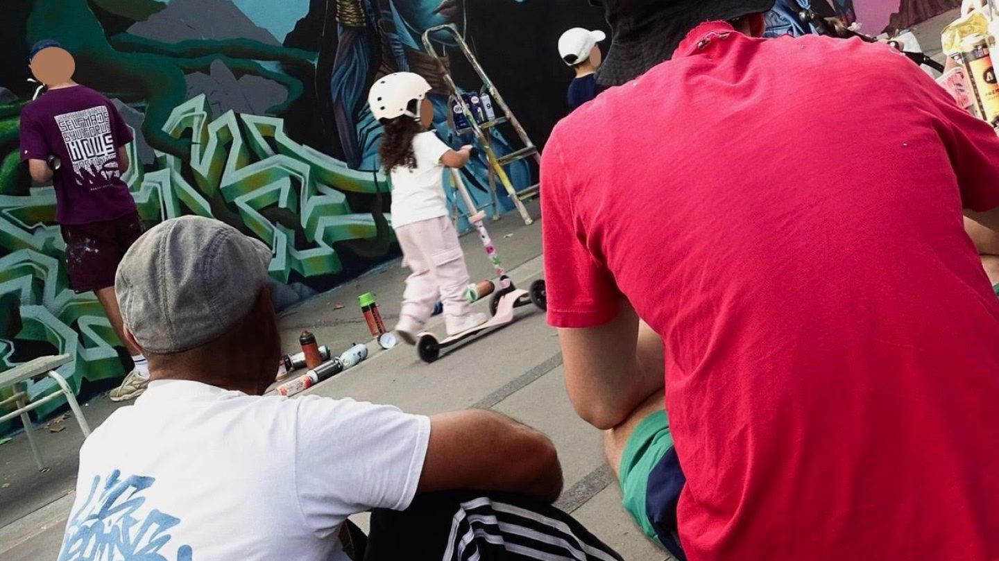 Public et artistes observant une fresque graffiti en cours avec ambiance conviviale