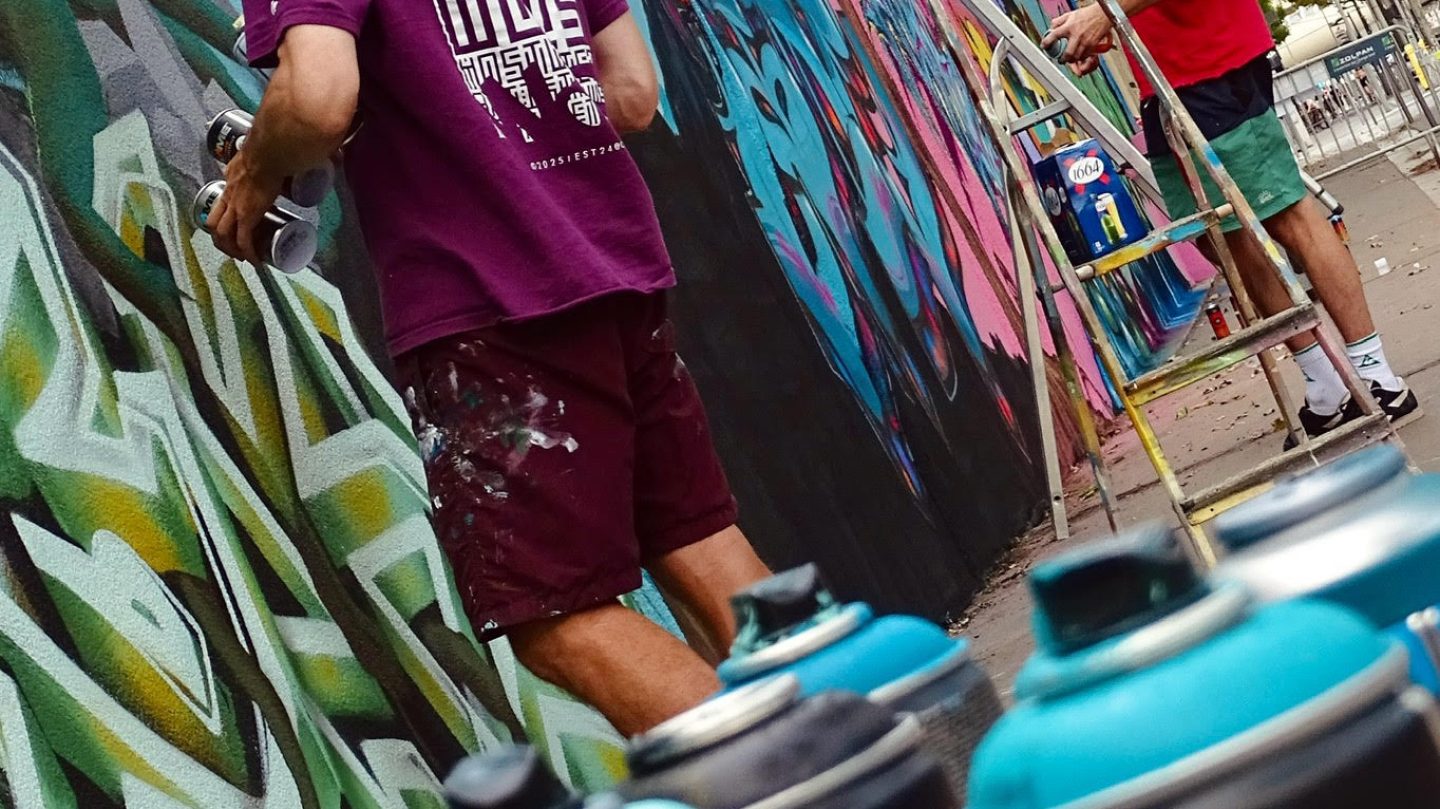 Bombes de peinture au premier plan avec artistes réalisant une fresque graffiti en arrière-plan