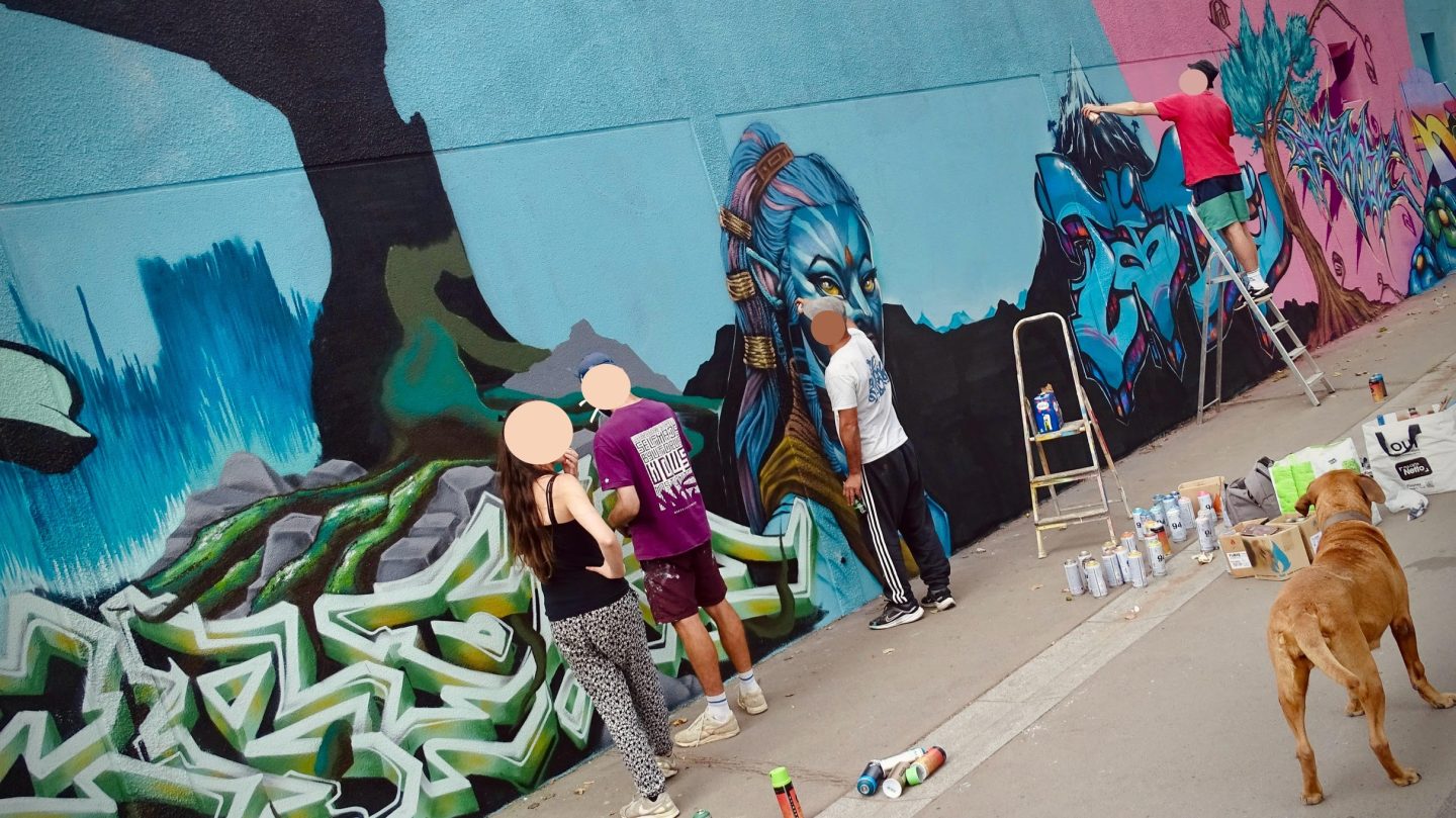 Plusieurs personnes observant et participant à une fresque street art avec un chien au premier plan