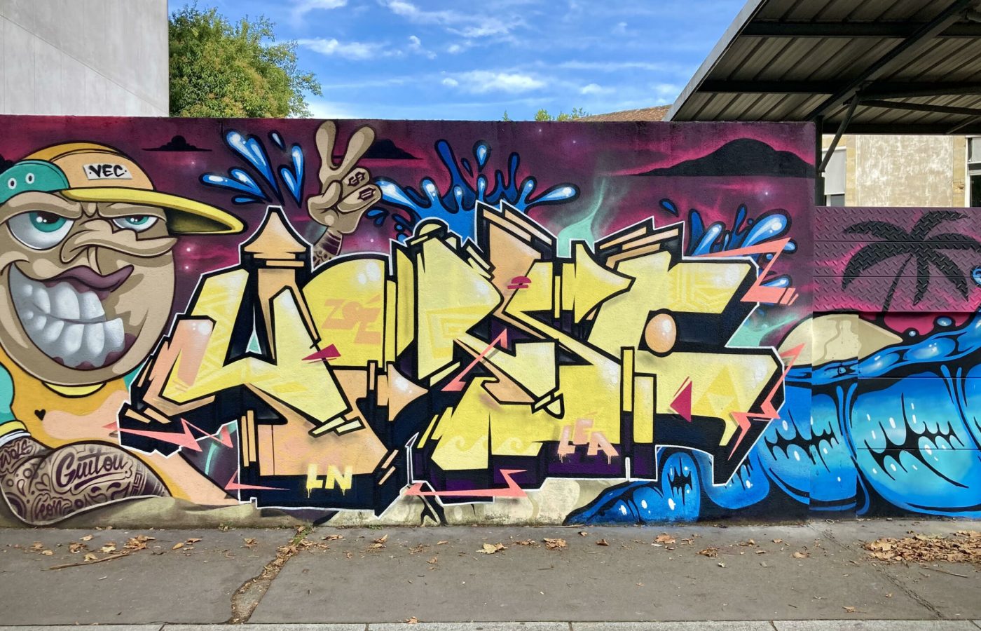 Fresque graffiti collaborative avec lettrage jaune et effets graphiques colorés.