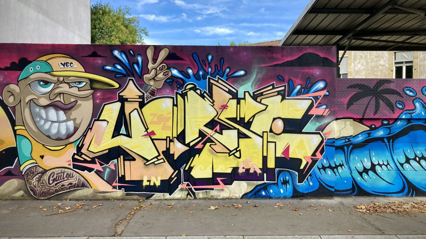 Fresque graffiti collaborative avec lettrage jaune et effets graphiques colorés.