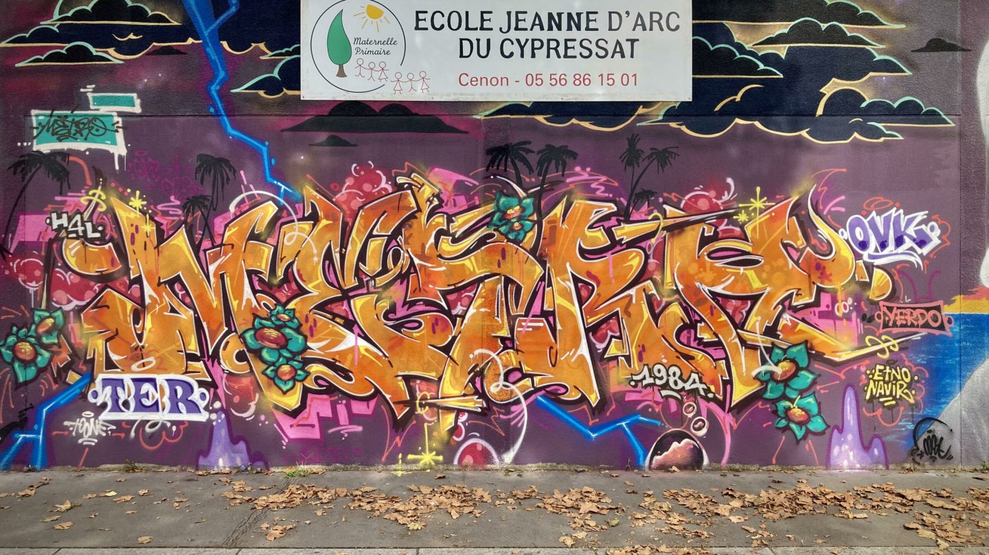 Fresque graffiti colorée avec lettrage dynamique sur mur d’école à Cenon.