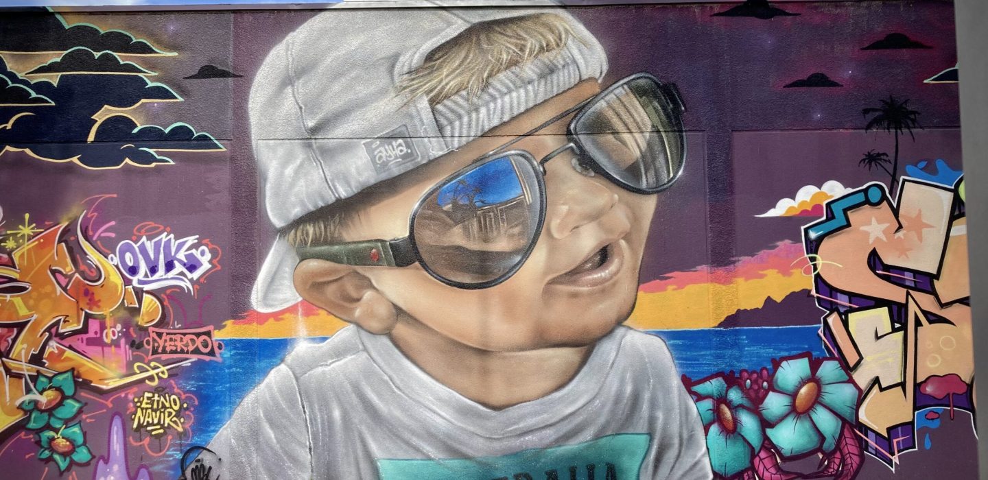 Portrait graffiti réaliste d’un enfant avec lunettes de soleil sur fresque Laguna Beach réalisée lors de la JAM D’ARC 2024 à Cenon.