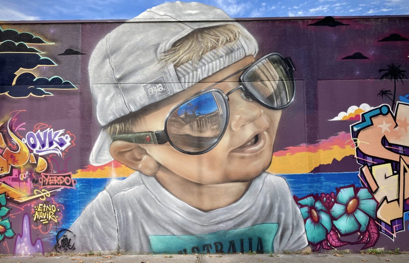 Portrait graffiti réaliste d’un enfant avec lunettes sur fond tropical.