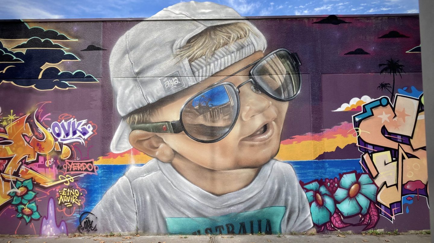 Portrait graffiti réaliste d’un enfant avec lunettes sur fond tropical.