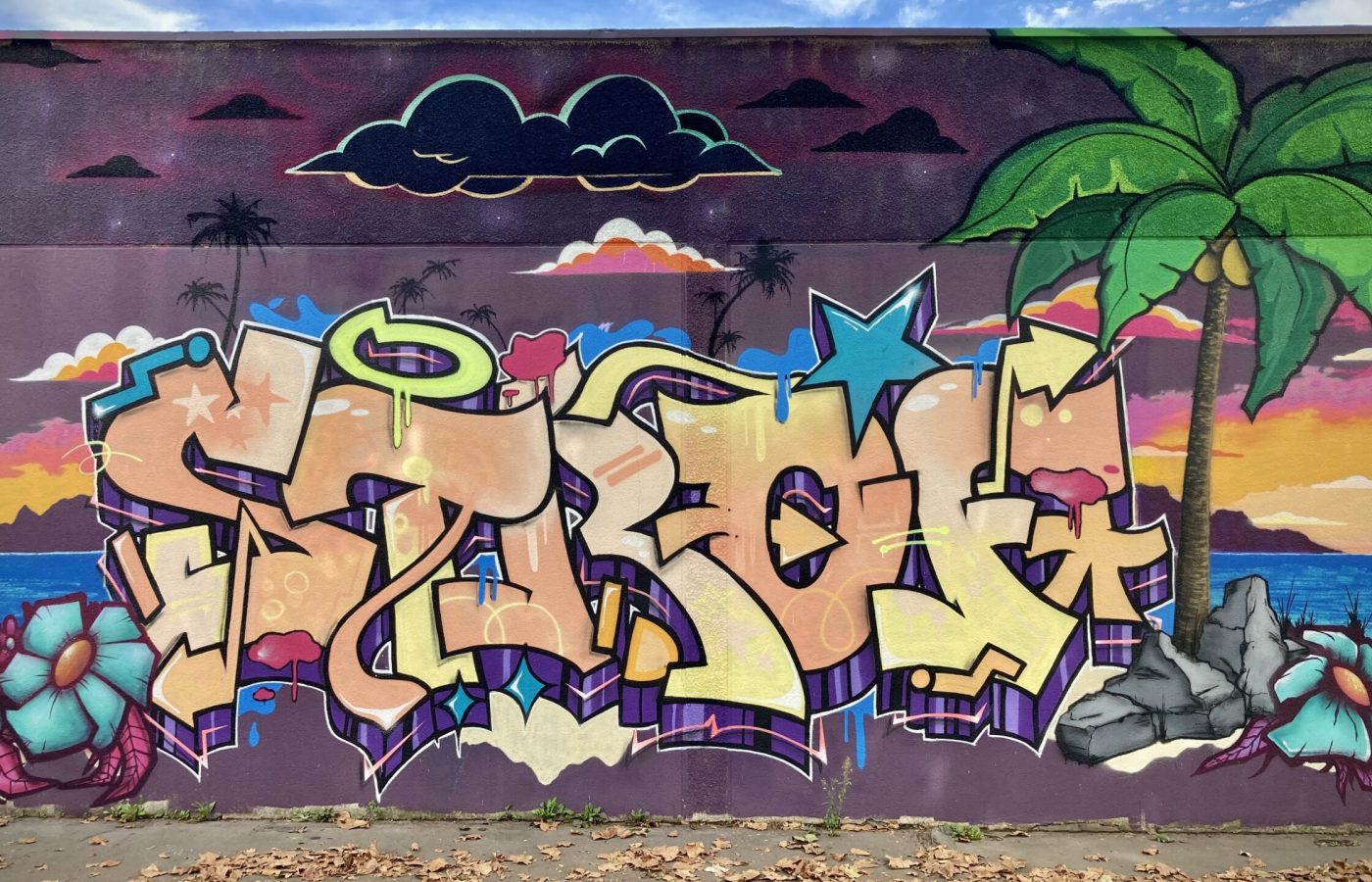 Lettrage graffiti avec fond coucher de soleil tropical et éléments colorés.