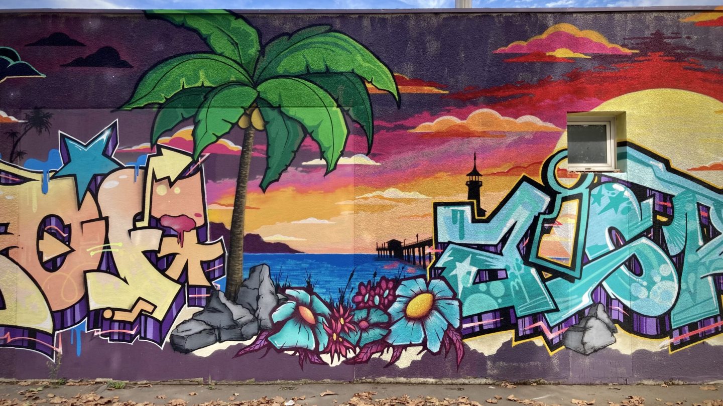 Fresque graffiti avec palmier, océan et lettrage coloré.