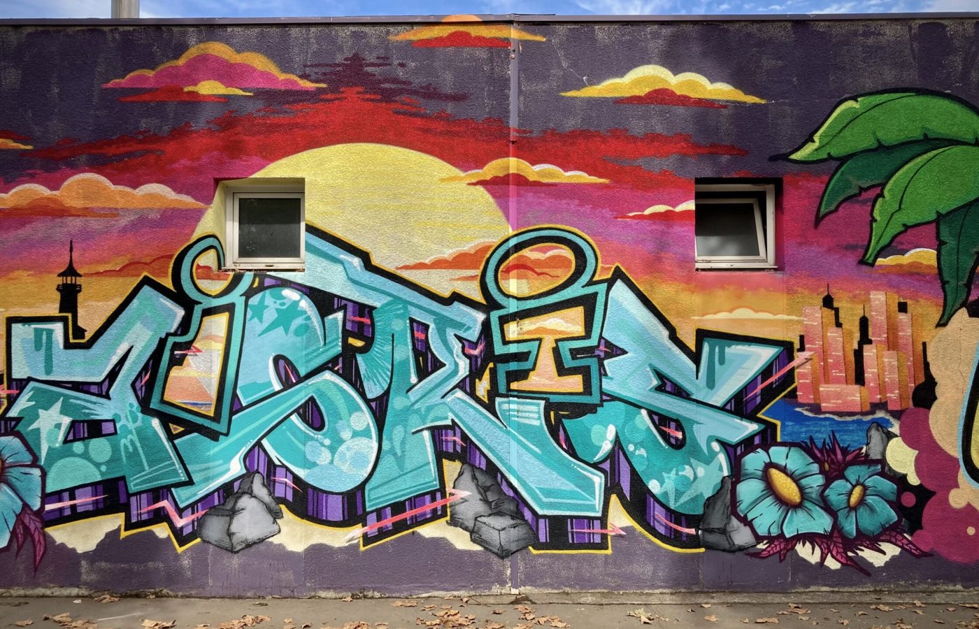 Lettrage graffiti bleu avec skyline et coucher de soleil en arrière-plan.