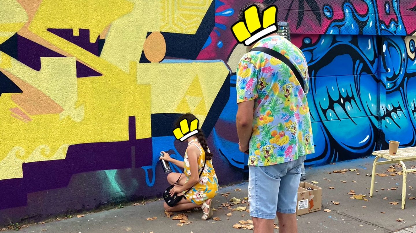 Une enfant apprend le graffiti encadrée par un artiste lors d’une fresque.