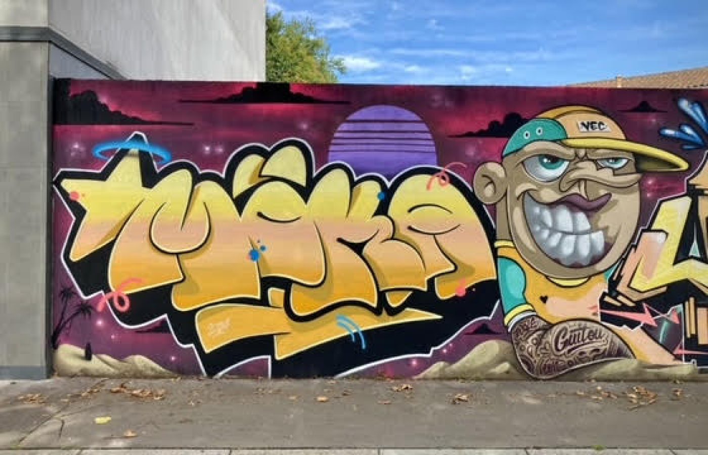 Fresque graffiti avec lettrage jaune et personnage cartoon réalisée à Cenon.