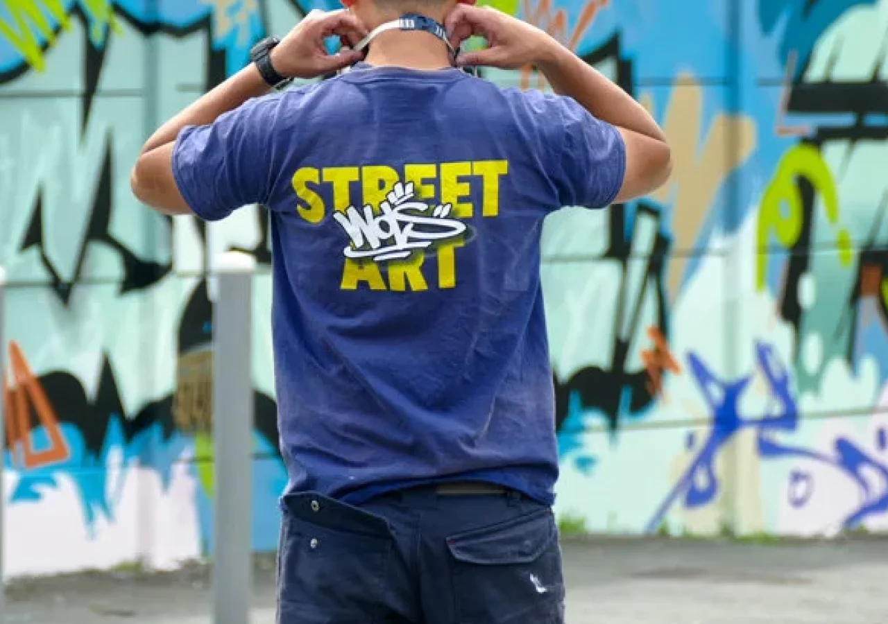 Artiste de dos portant un t-shirt WOLS Street Art devant une fresque graffiti lors de l’événement SLATE 25 à Cenon.
