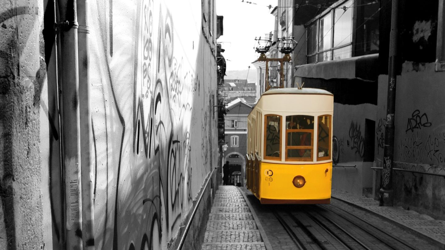 Funiculaire jaune circulant dans une rue urbaine couverte de graffitis et de street art au Portugal.