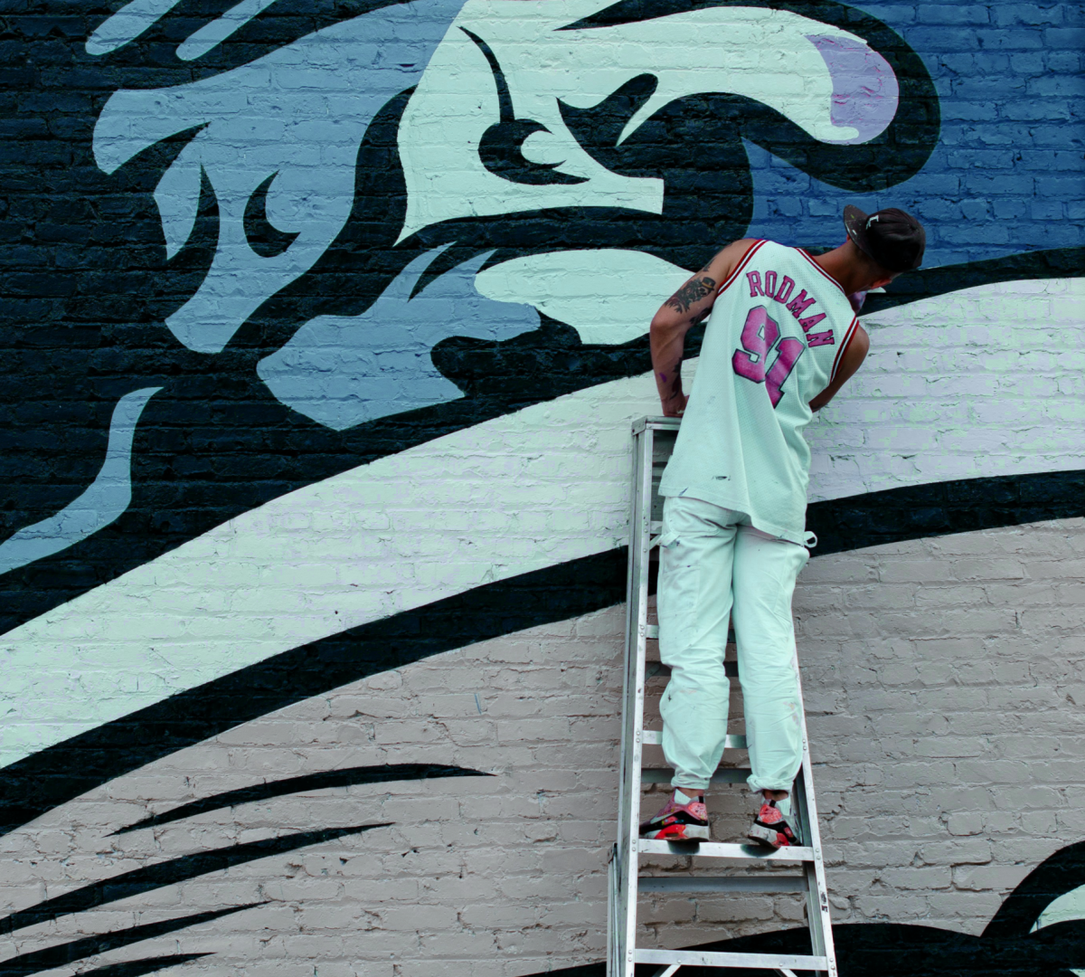 Street artist peignant une fresque murale, debout sur une échelle.