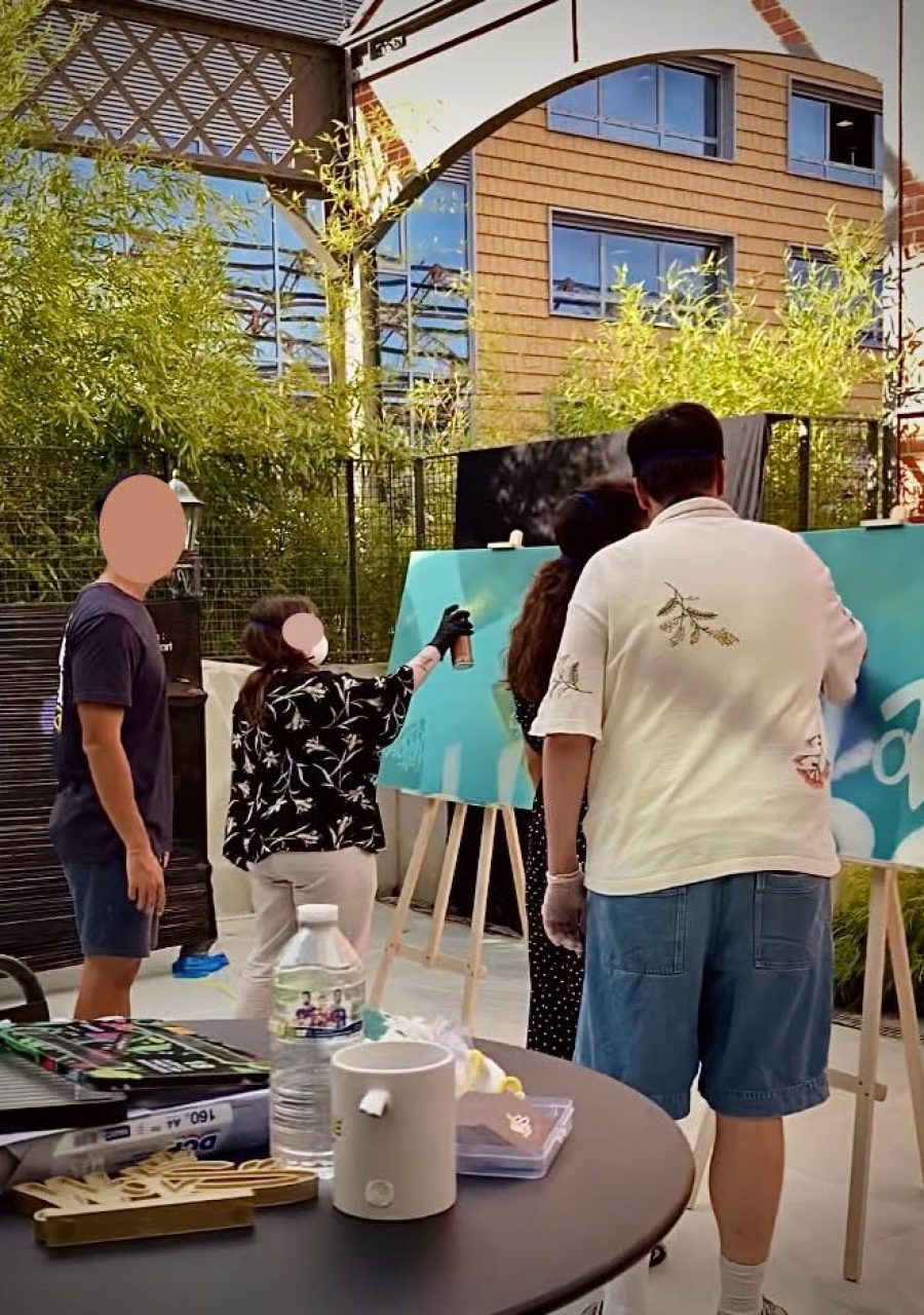 Employés d’Ubisoft Bordeaux peignant à la bombe sur des toiles lors d’un atelier graffiti collaboratif animé par WOLS Street Art.