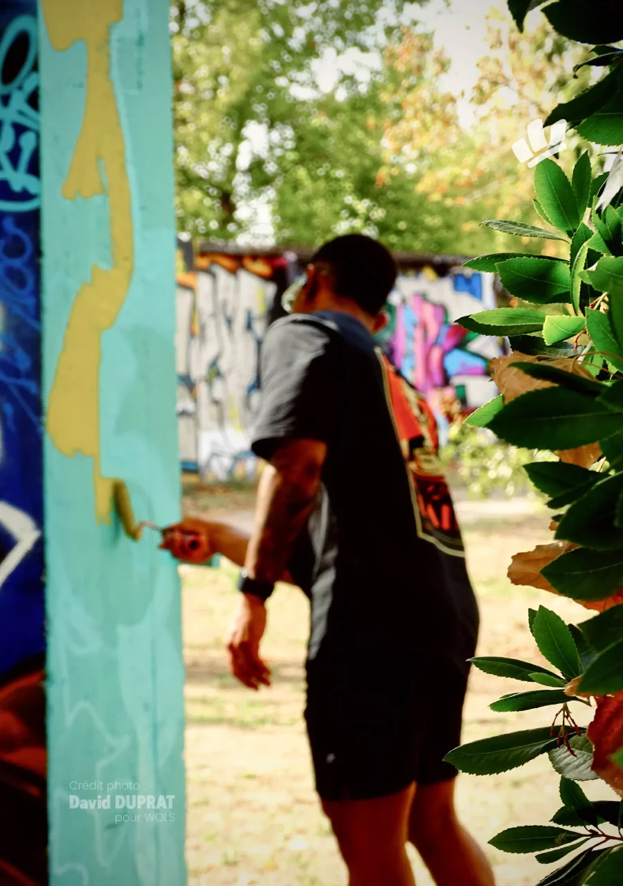 Graffeur peignant un mur turquoise au rouleau lors du WOLS Open Spray #2.