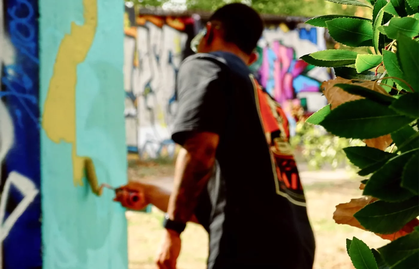 Graffeur peignant un mur turquoise au rouleau lors du WOLS Open Spray #2.