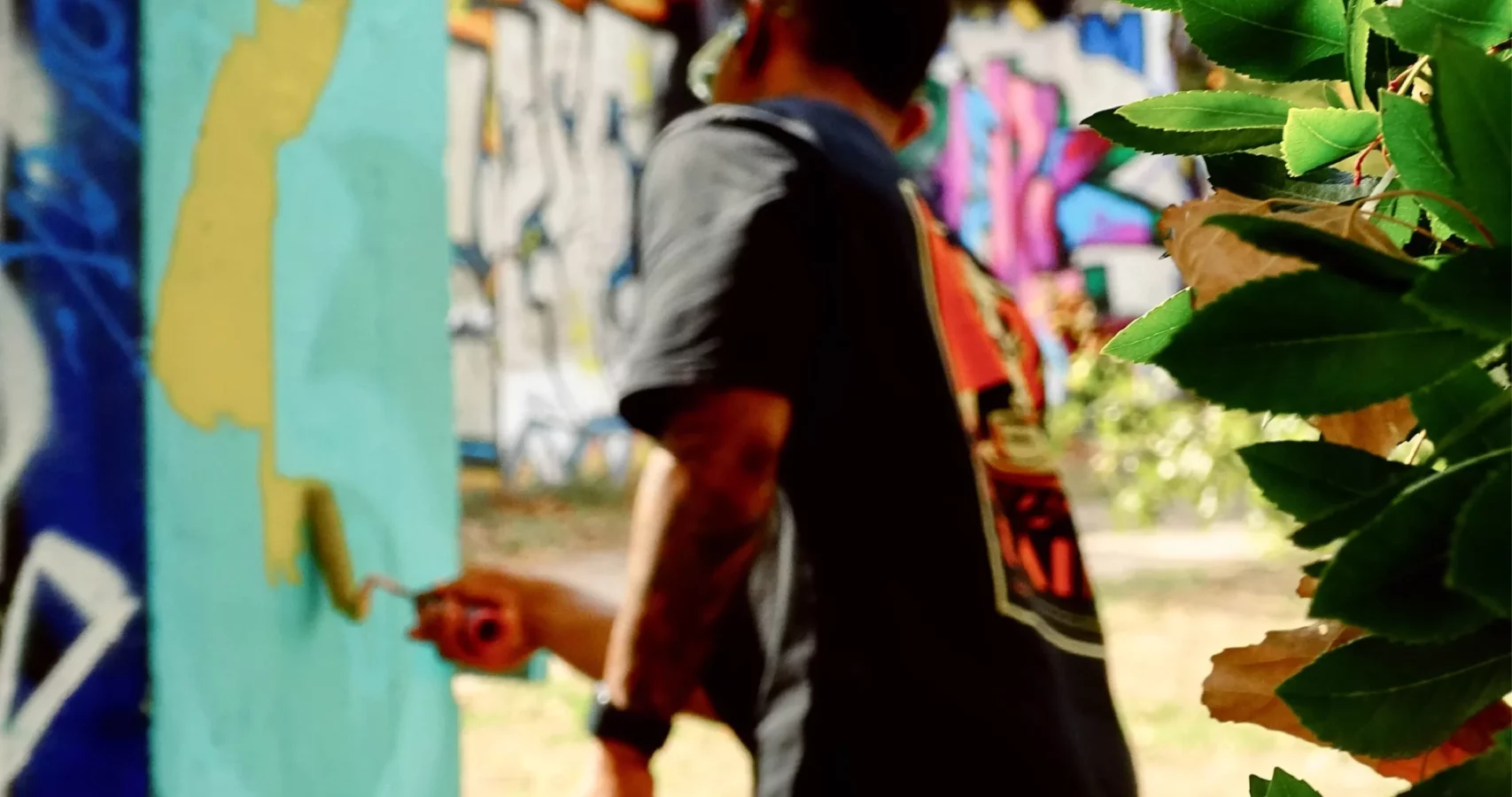 Graffeur peignant un mur turquoise au rouleau lors du WOLS Open Spray #2.