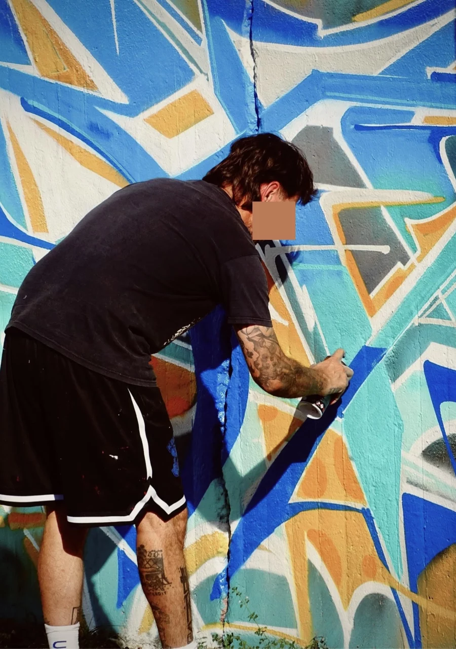 Graffeur réalisant une fresque géométrique bleue et orange à la bombe de peinture lors du WOLS Open Spray.