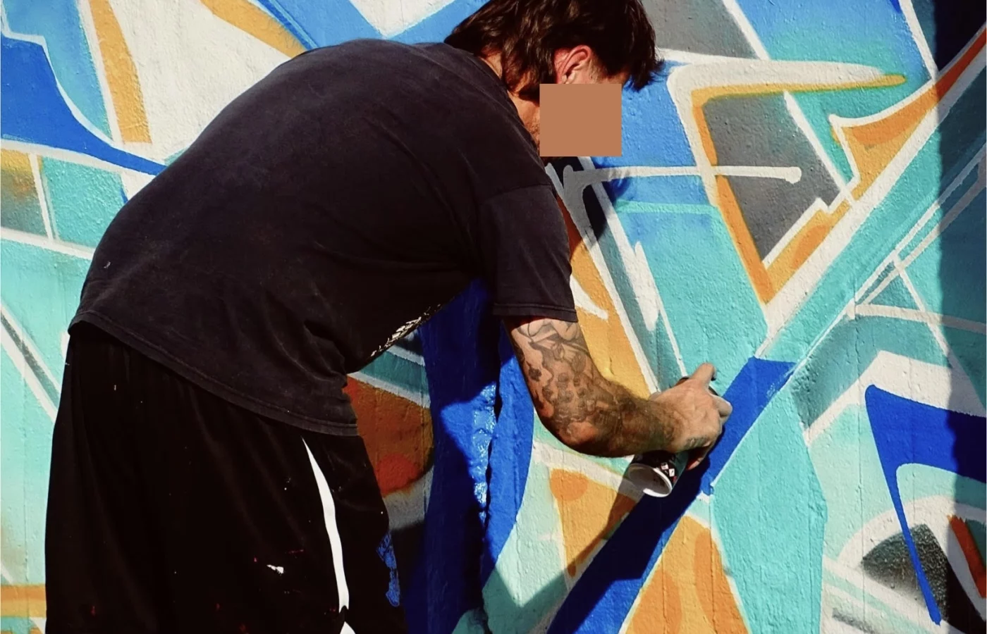 Graffeur réalisant une fresque géométrique bleue et orange à la bombe de peinture lors du WOLS Open Spray.