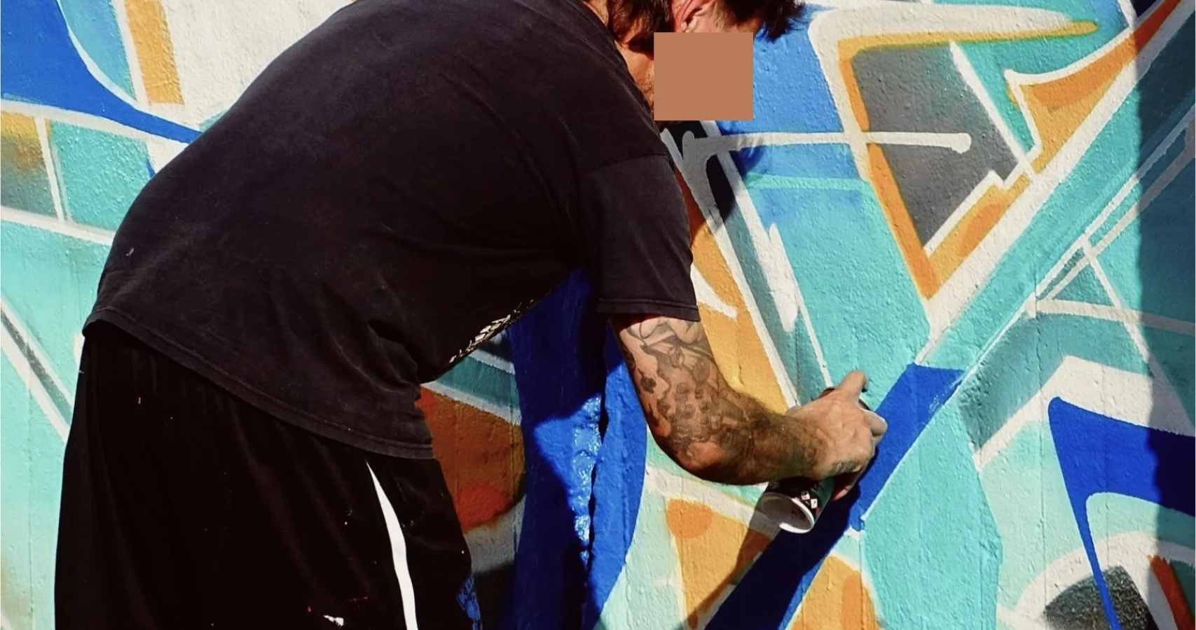 Graffeur réalisant une fresque géométrique bleue et orange à la bombe de peinture lors du WOLS Open Spray.