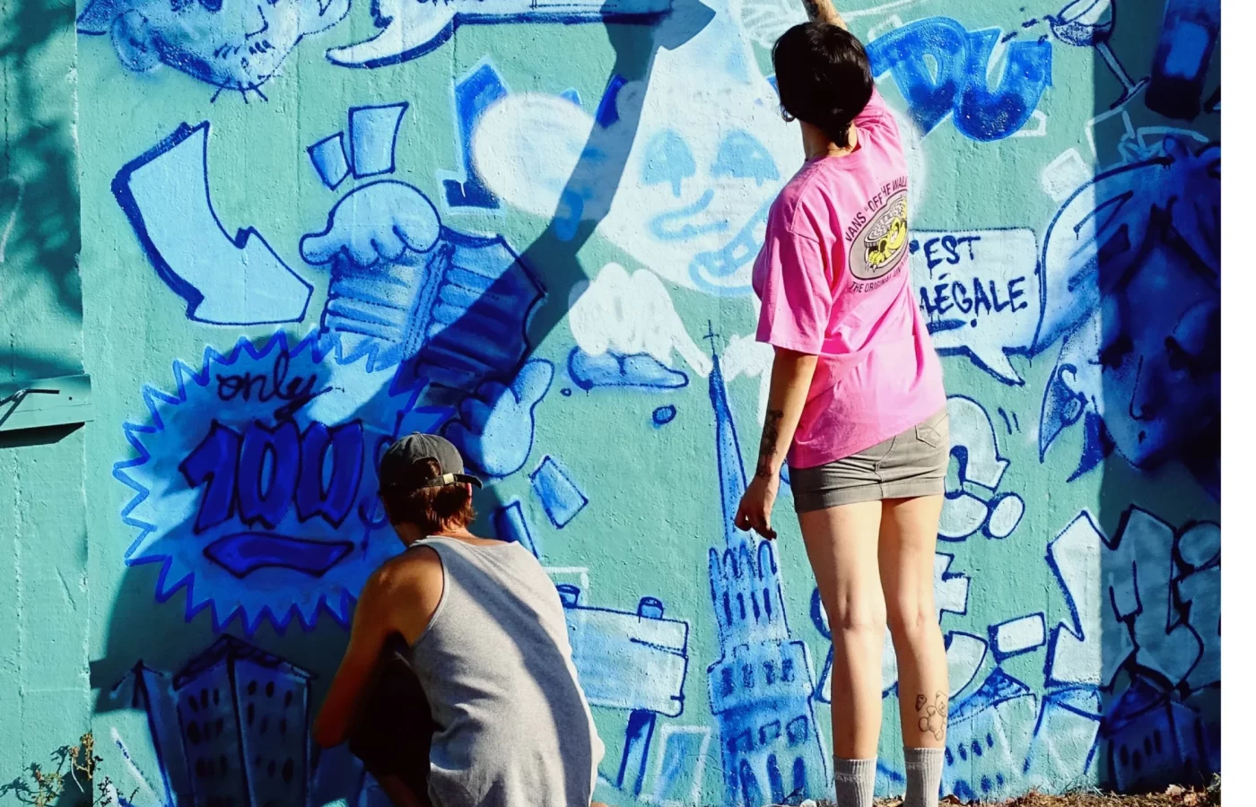 Deux participants peignant à la bombe un mur couvert de dessins et de graffiti lors du WOLS Open Spray #2.
