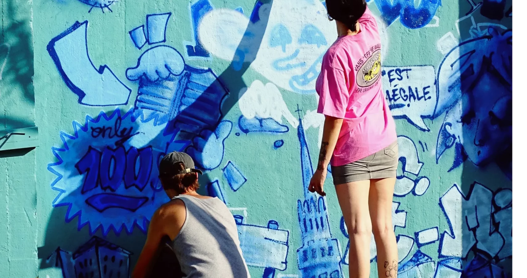 Deux participants peignant à la bombe un mur couvert de dessins et de graffiti lors du WOLS Open Spray #2.