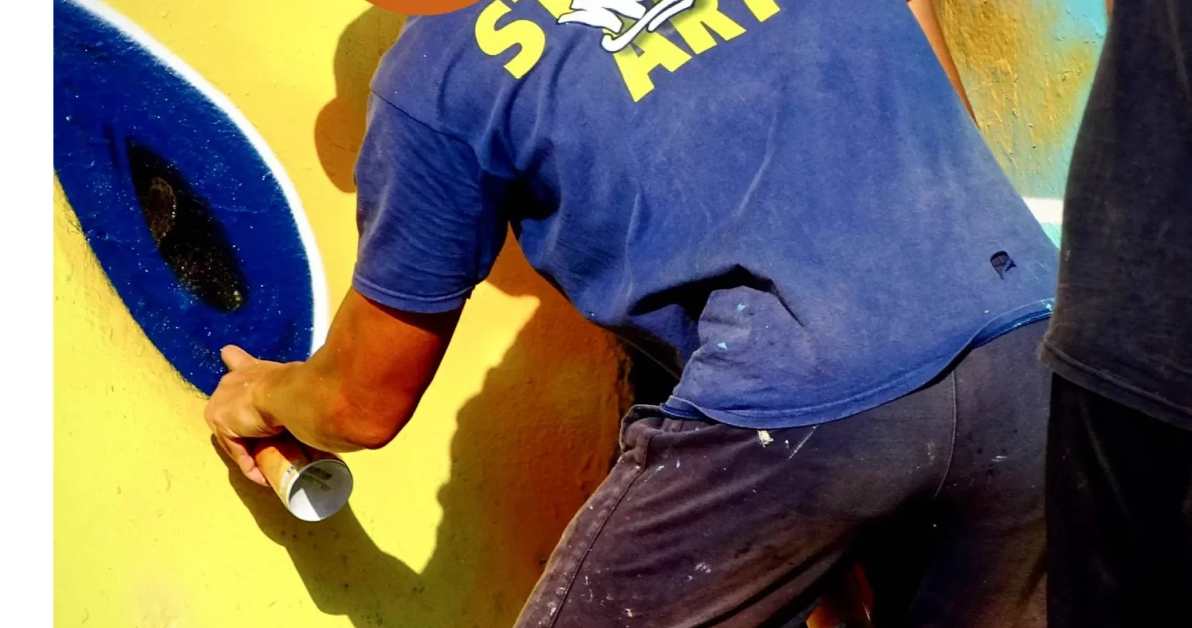 Graffeur peignant à la bombe une fresque jaune et bleue lors du WOLS Open Spray #2.