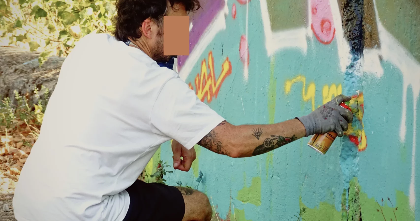 Graffeur accroupi peignant à la bombe les détails d’une fresque lors du WOLS Open Spray #2.