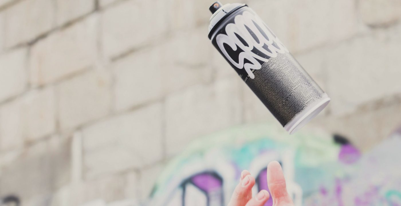 Main lançant une bombe de peinture graffiti en l’air devant mur street art