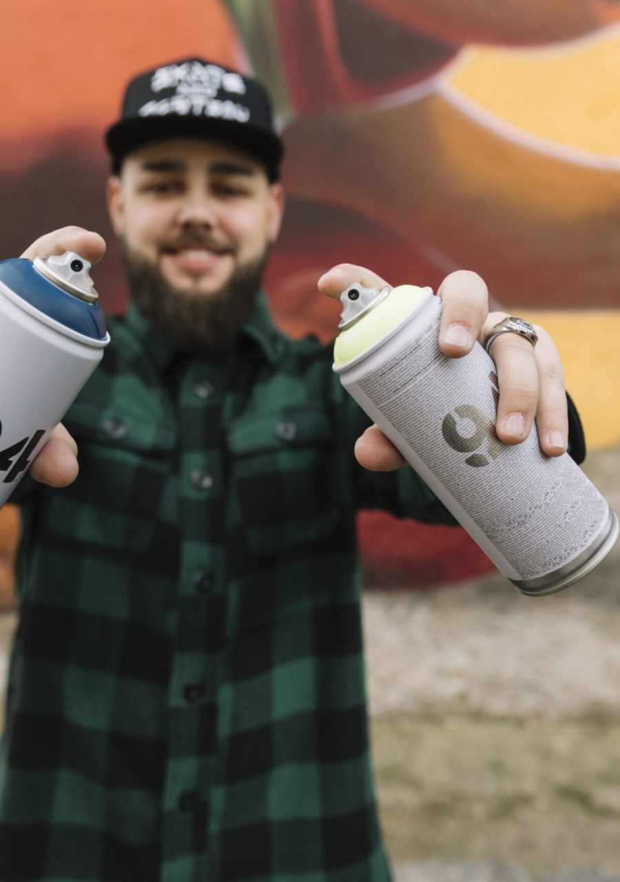 Artiste graffiti présentant des bombes de peinture aérosol devant une fresque street art