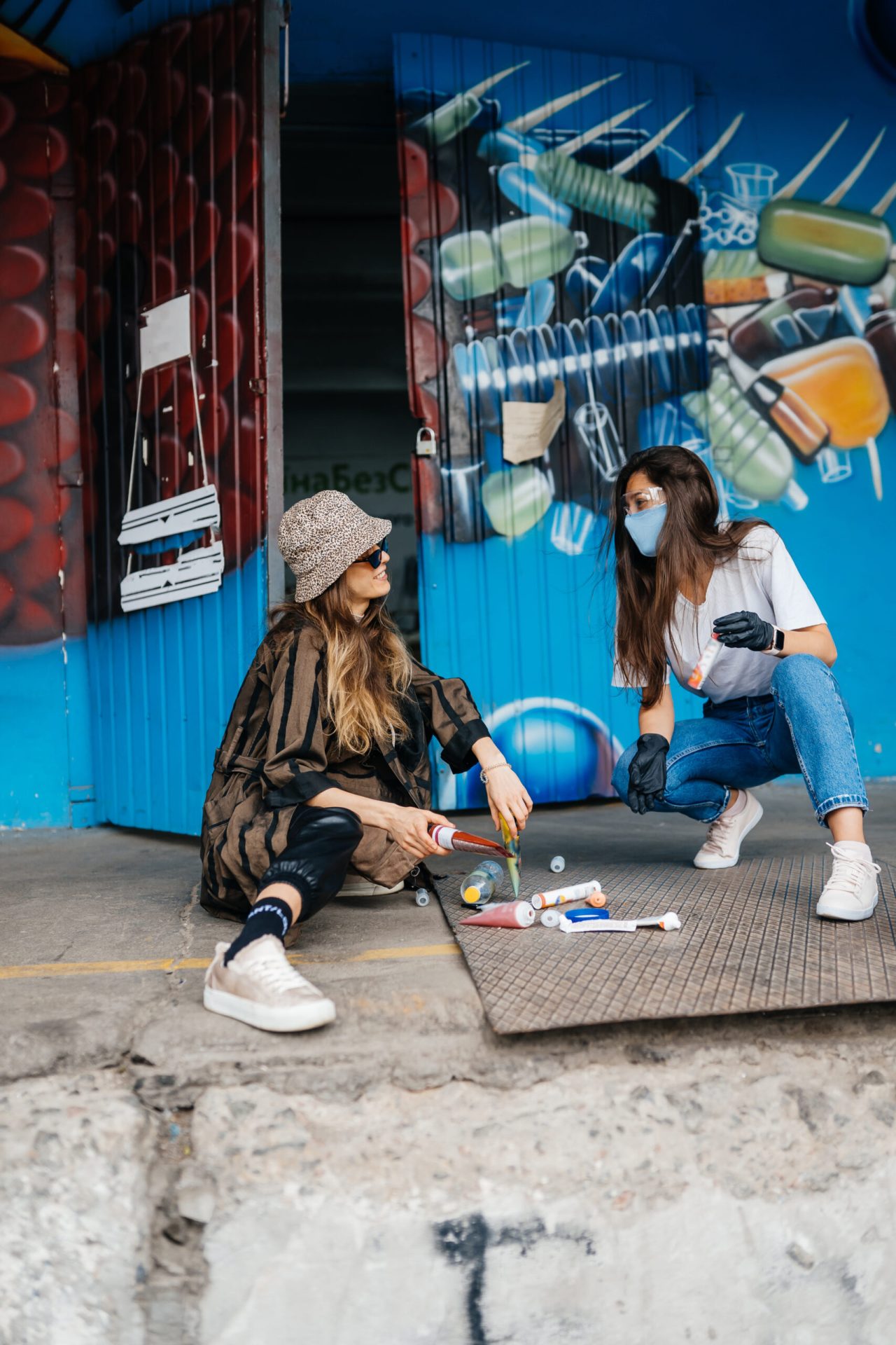 Deux artistes street art préparant des bombes de peinture devant une fresque urbaine colorée